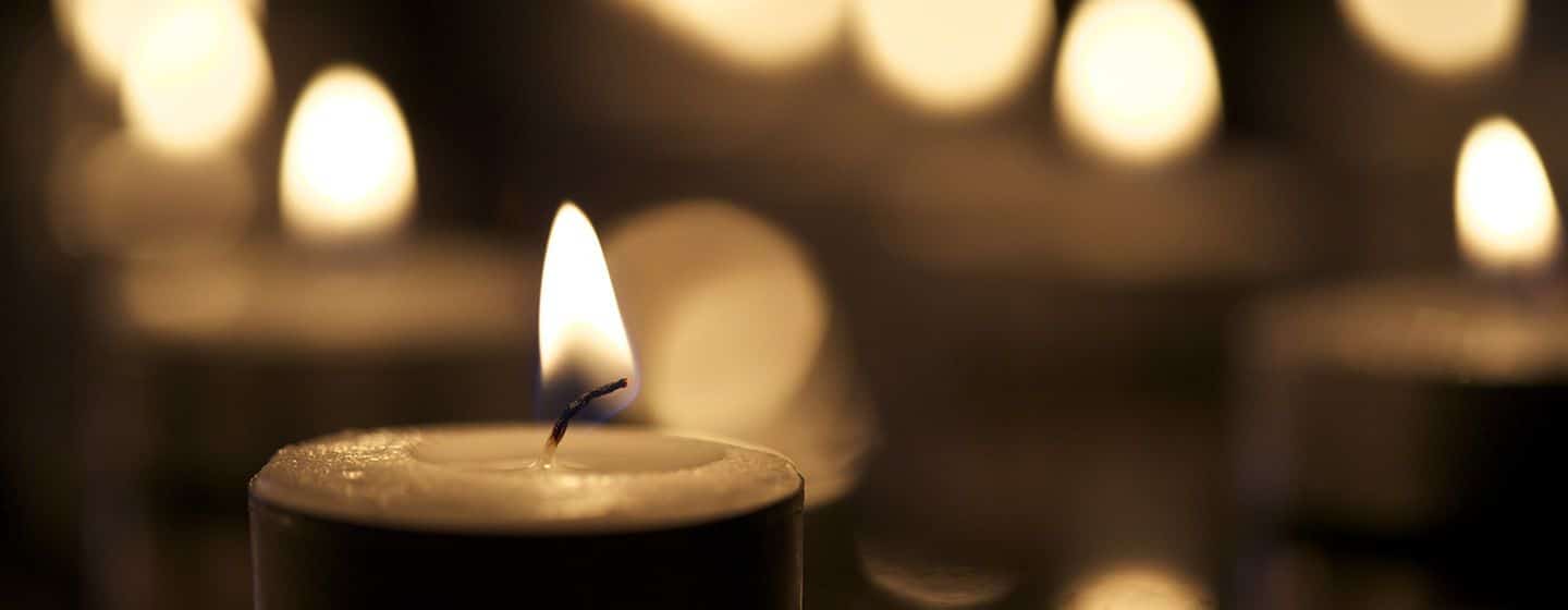 Single tea candle against a blurred background of multiple candles.