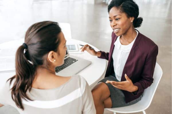 A woman sitting down with a lawyer at a white table with white chairs, discussing the fees for personal injury representation.