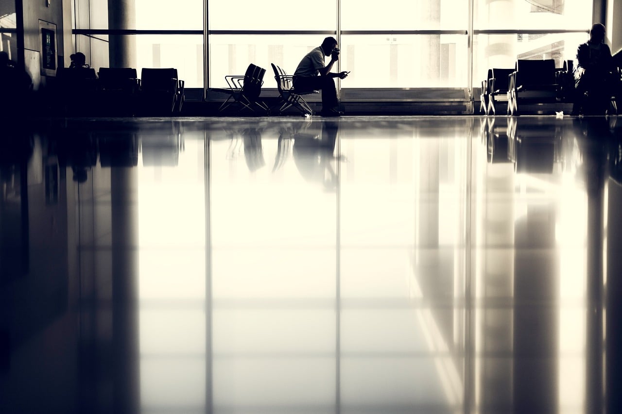 Man silhouetted against airport window sitting in terminal